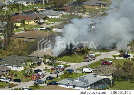 View from above of burning private house on fire and firefighters extinguishing flames after short circuit caused to ignite roof damaged by hurricane Ian wind. Home disaster in Florida suburban area View from above of burning private house on fire and firefighters extinguishing flames after short circuit caused to ignite roof damaged by hurricane Ian wind. Home disaster in Florida suburban area 106991303