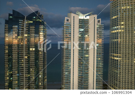 View from above of brightly illuminated high skyscraper buildings in downtown district of Sunny Isles Beach city in Florida, USA. American tourist urban district at night View from above of brightly illuminated high skyscraper buildings in downtown district of Sunny Isles Beach city in Florida, USA. American tourist urban district at night 106991304