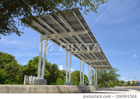 Solar panels installed as shade roof over parking lot for parked electric cars for effective generation of clean electricity. Photovoltaic technology integrated in urban infrastructure Solar panels installed as shade roof over parking lot for parked electric cars for effective generation of clean electricity. Photovoltaic technology integrated in urban infrastructure 106991568