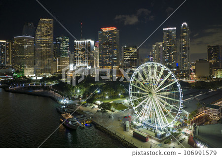 Skyviews Miami Observation Wheel at Bayside Marketplace with reflections in Biscayne Bay water and high illuminated skyscrapers of Brickell, city's financial center Skyviews Miami Observation Wheel at Bayside Marketplace with reflections in Biscayne Bay water and high illuminated skyscrapers of Brickell, city's financial center 106991579