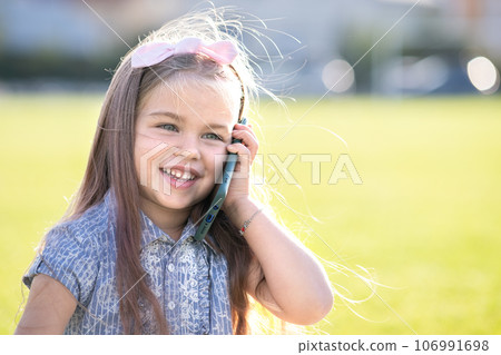 Pretty little child girl speaking on mobile phone smiling happily outdoors in summer. Pretty little child girl speaking on mobile phone smiling happily outdoors in summer. 106991698