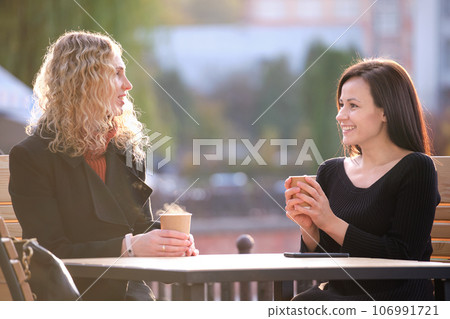 Portrait of two happy young women sitting at city street cafe Portrait of two happy young women sitting at city street cafe 106991721