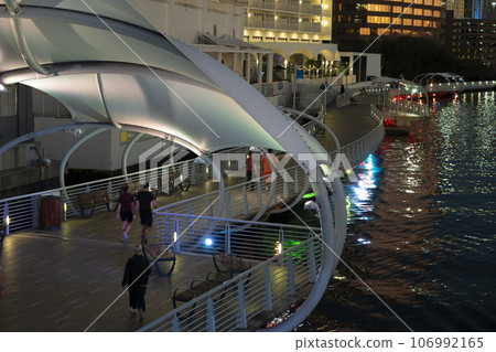 People walking on pedestrian riverwalk trail alongside river water in downtown district of Tampa city in Florida, USA. Recreational area in modern american megapolis 106992165