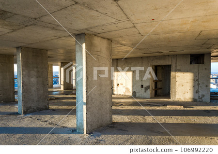 Interior of a concrete residential apartment building room with unfinished bare walls and support pillars for future walls under construction. 106992220