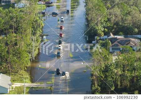Hurricane flooded street with moving cars and surrounded with water houses in Florida residential area. Consequences of natural disaster Hurricane flooded street with moving cars and surrounded with water houses in Florida residential area. Consequences of natural disaster 106992230