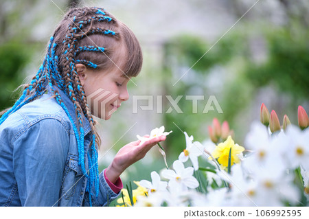 Happy child girl playing in summer garden enjoying sweet scent of white narcissus flowers on sunny day 106992595