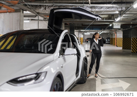 Female speaking on phone while refueling e-car in parking 106992671
