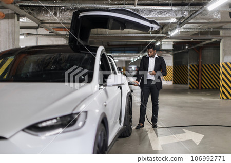 Man inserting charger gun in EV pot in public parking garage 106992771