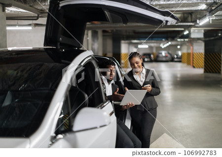 Partners operating laptop while sitting in EV in parking 106992783