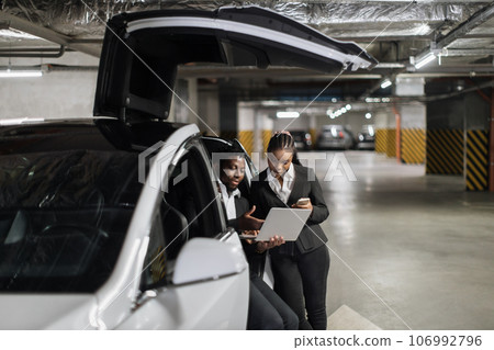 Partners operating laptop while sitting in EV in parking 106992796