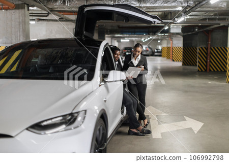 Partners operating laptop while sitting in EV in parking 106992798