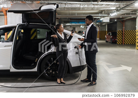 People with mobiles discussing issues while EV recharging People with mobiles discussing issues while EV recharging 106992879