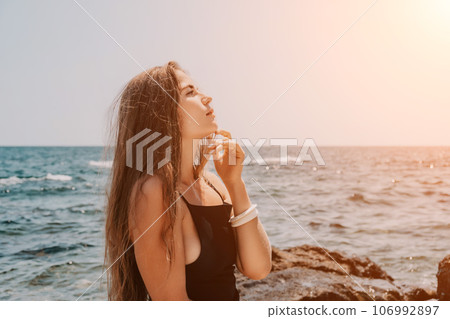 Woman summer travel sea. Happy tourist in hat enjoy taking picture outdoors for memories. Woman traveler posing on the beach at sea surrounded by volcanic mountains, sharing travel adventure journey 106992897