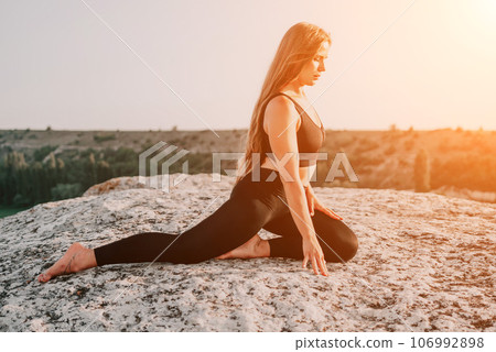 Fitness woman. Happy middle-aged fitness woman doing stretching and pilates on a rock near forest at sunset. Female fitness yoga routine. Healthy lifestyle with focus on well-being and relaxation. 106992898