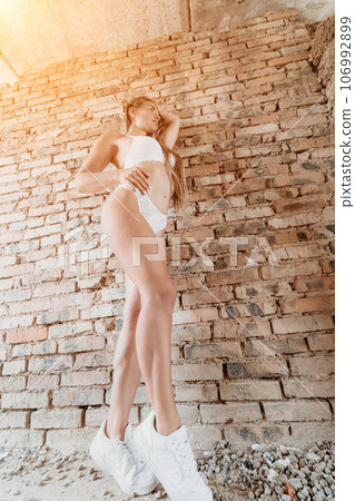 A mid-30s happy woman with long hair natural color poses in her underwear, smiling in front of a brick wall on a construction site for model tests 106992899