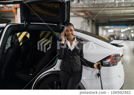 Worker listening to phone caller while filling up EV indoors Worker listening to phone caller while filling up EV indoors 106992982