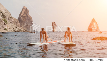 Woman sup yoga. Happy sporty woman practising yoga pilates on paddle sup surfboard. Female stretching doing workout on sea water. Modern individual female hipster outdoor summer sport activity. Woman sup yoga. Happy sporty woman practising yoga pilates on paddle sup surfboard. Female stretching doing workout on sea water. Modern individual female hipster outdoor summer sport activity. 106992983