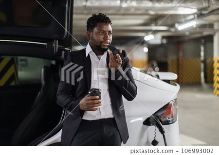 Adult with drink recording audio on mobile during EV charge Adult with drink recording audio on mobile during EV charge 106993002