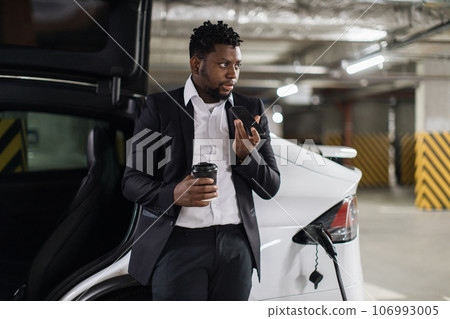 Adult with drink recording audio on mobile during EV charge Adult with drink recording audio on mobile during EV charge 106993005