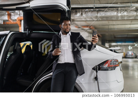 Worker with drink taking selfie near EV in basement parking Worker with drink taking selfie near EV in basement parking 106993013