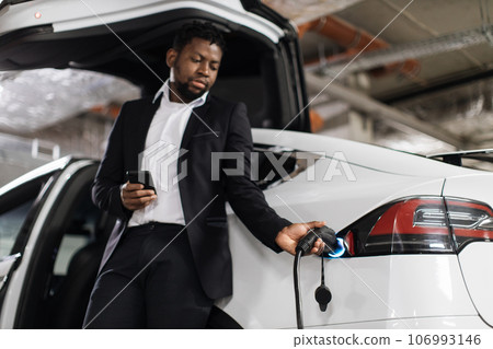 Employee with mobile starting EV charging session in parking Employee with mobile starting EV charging session in parking 106993146
