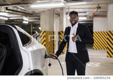 Worker using charging cable for e-car in basement garage Worker using charging cable for e-car in basement garage 106993230