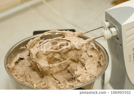 Closeup of electrical blender whipping in bowl chocolate cream for cake, ice cream or dessert. Kitchen bakery equipment, homemade baking. 106993502