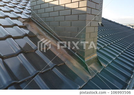 Closeup of brick chimney on house roof top covered with ceramic shingles. Tiled covering of building Closeup of brick chimney on house roof top covered with ceramic shingles. Tiled covering of building 106993506