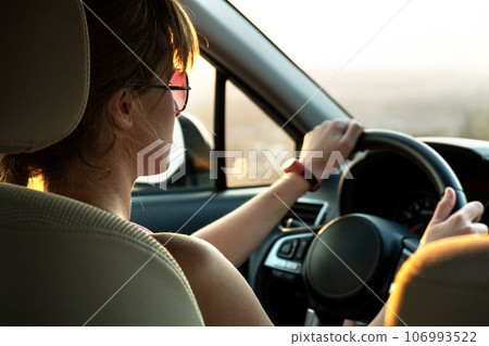 Close up view of a woman driver holding steering wheel driving a car at sunset. 106993522