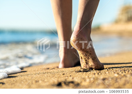 Close up of woman feet walking barefoot on sand leaving footprints on golden beach. Vacation, travel and freedom concept. People relaxing in summer. 106993535