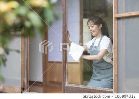 A young woman wiping the window of an old folk house A young woman wiping the window of an old folk house 106994312