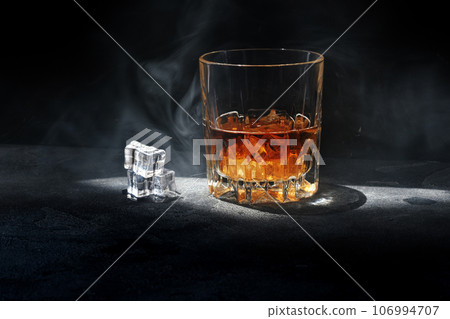 Whiskey with smoke on dark background and ice cubes 106994707