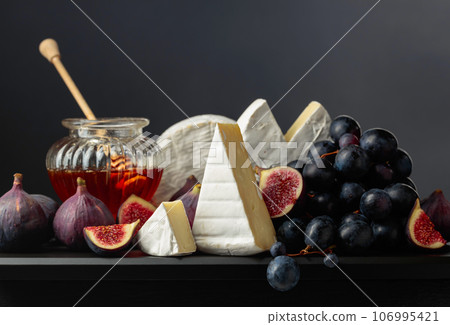 Camembert cheese with fruits and honey on a black background. 106995421