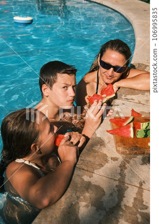 mom and kids eat watermelon in the pool mom and kids eat watermelon in the pool 106995835