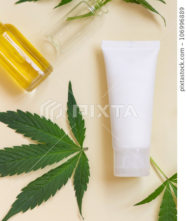 Cream tube near green cannabis leaves top view on beige, CBD cosmetics 106996889
