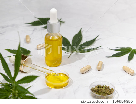 Dropper bottle with CBD oil, pipette and capsules near cannabis leaves close up, hard shadows 106996890