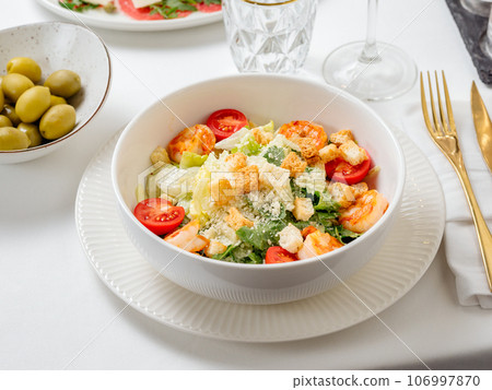 Caesar salad with shrimps on plate in restaurant table interior. Classic caesar shrimp salad closeup view 106997870