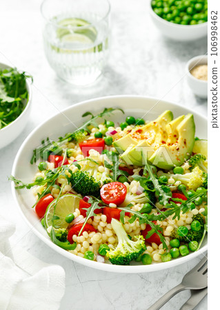 Couscous salad with broccoli, green peas, tomatoes, avocado and fresh arugula. Healthy natural plant based vegetarian food for lunch, israeli cuisine 106998462