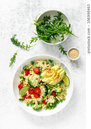 Couscous salad with broccoli, green peas, tomatoes, avocado and fresh arugula. Healthy natural plant based vegetarian food for lunch, israeli cuisine, top view 106998463