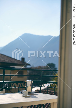 Italian coffee maker and a cup of espresso on the table, on balcony overlooking a mesmerizing landscape of Italian Alps 106999342