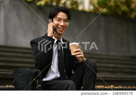 Smiling businessman sitting on stairs outside office building and talking on mobile phone. Technology and communication Smiling businessman sitting on stairs outside office building and talking on mobile phone. Technology and communication 106999579