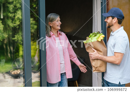 Grocery store delivery man delivering food to woman home. Grocery store delivery man delivering food to woman home. 106999872
