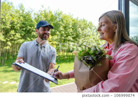 Courier service worker delivering fresh food to woman client signing some documents. Courier service worker delivering fresh food to woman client signing some documents. 106999874