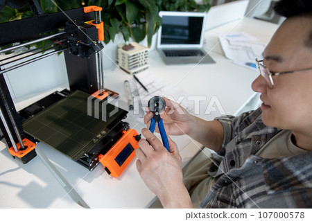Asian designer engineer using 3D printer in laboratory and studying product prototype. Asian designer engineer using 3D printer in laboratory and studying product prototype. 107000578