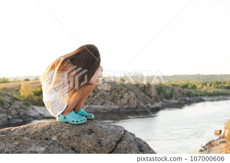 Offended five-year-old sad girl sitting on rocks in nature alone. Offended five-year-old sad girl sitting on rocks in nature alone. 107000606