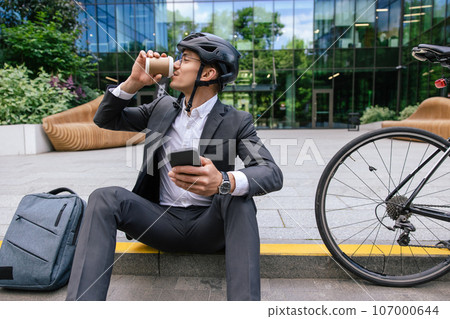 Man in hemlet having coffee after cycling to the office Man in hemlet having coffee after cycling to the office 107000644