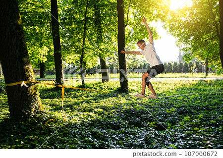 Man in sportswear doing slacklining in the forest Man in sportswear doing slacklining in the forest 107000672