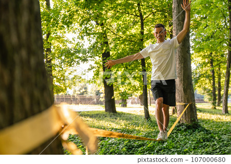 Man in sportswear doing slacklining in the forest Man in sportswear doing slacklining in the forest 107000680