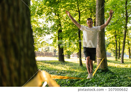 Young man balancing on the rope in the forest Young man balancing on the rope in the forest 107000682