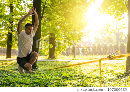 Young man balancing on the rope in the forest Young man balancing on the rope in the forest 107000683